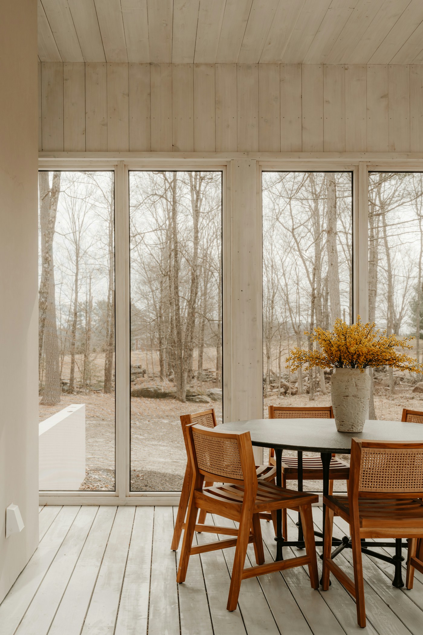 Shared dining table beside tall windows overlooking the woods