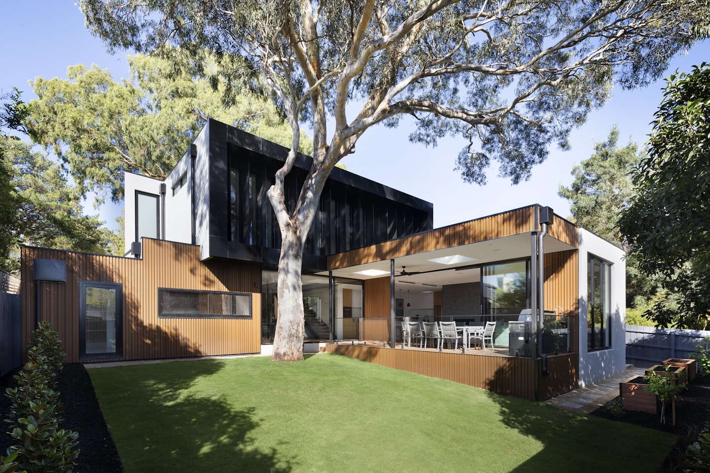 Black timber retreat opening from a broad lawn beneath mature trees