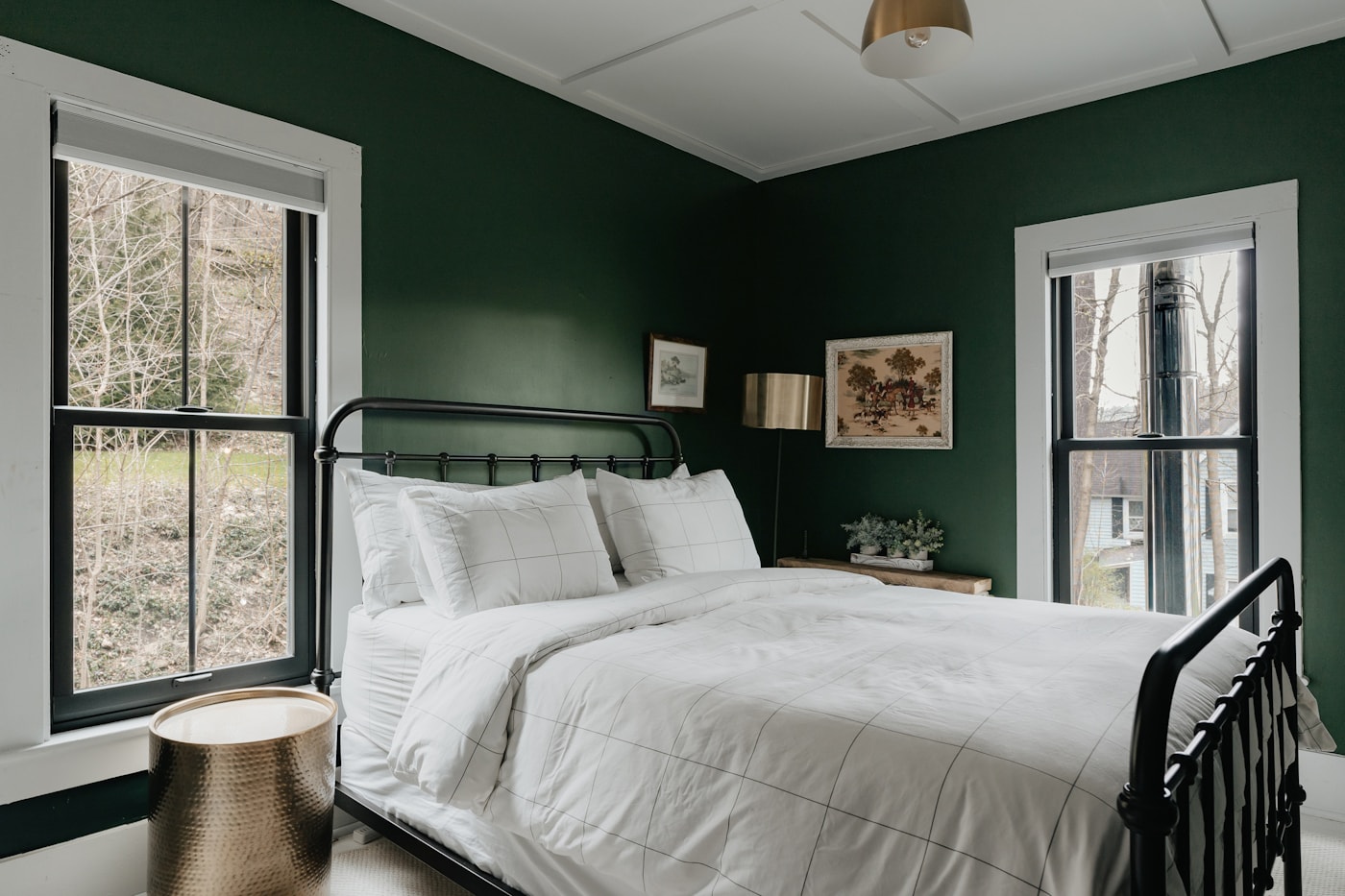 Green guest room with crisp white bedding and windows facing the woods